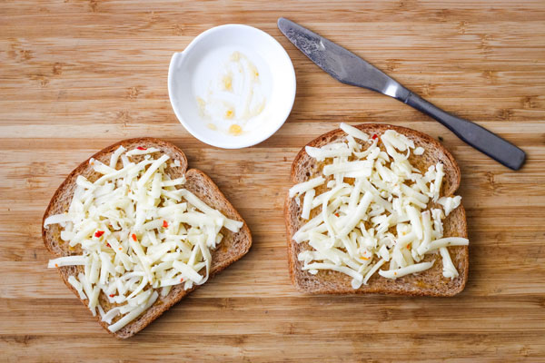 Two slices of bread topped with preserves and shredded cheese on a cutting board.