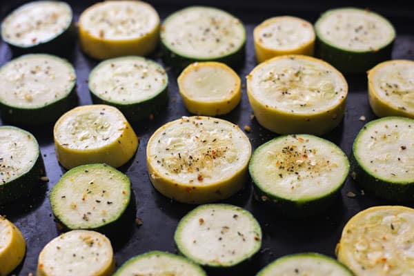 Seasoned zucchini slices on a black roasting pan.