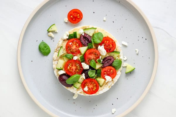 Rice cake topped with chopped vegetables, feta, and olives.