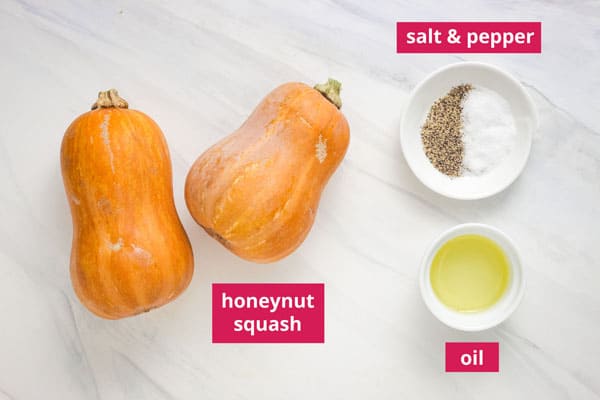 Two small honeynut squash and ramekins with salt and pepper and oil labeled on a table.