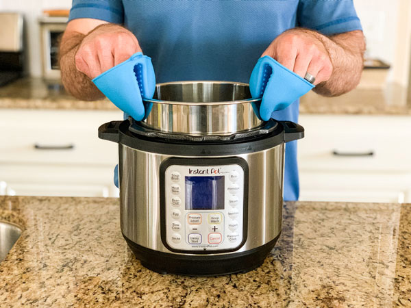 Hands using silicone mittens to remove pot from instant pot machine.