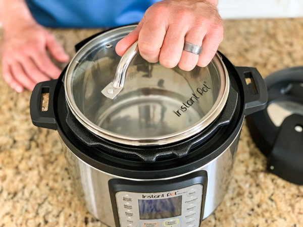 Hand holding a glass lid on top of a 3-Quart Instant Pot.