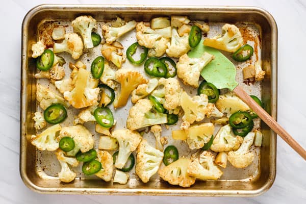 Pan of roasting cauliflower stirred with a green rubber spatula.