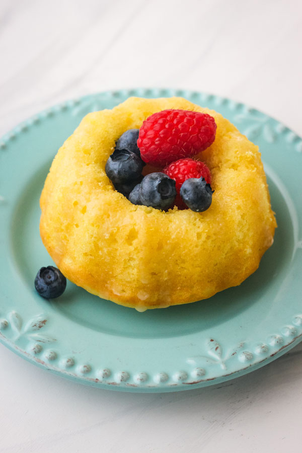 A small blue plate with a mini lemon bundt cake topped with fresh blueberries and raspberries.