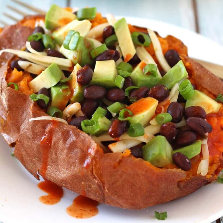 Sweet potato topped with black beans, cheese, and avocado on a plate.