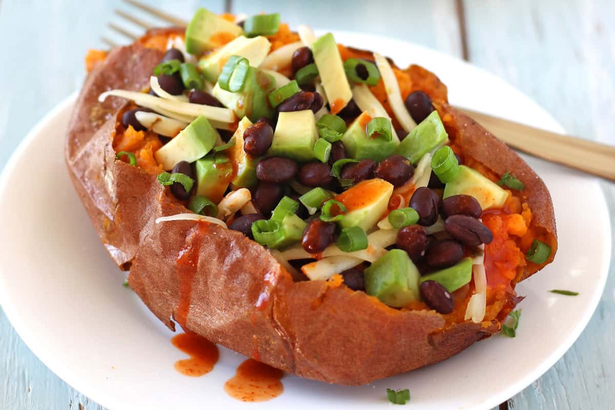 Sweet potato topped with black beans, cheese, and avocado on a plate.