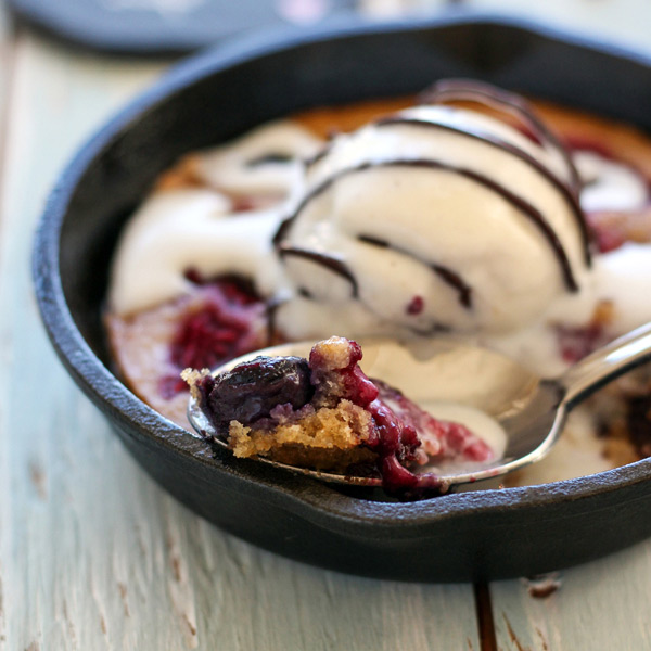 Close up of spoon with scoop of juicy berries, ice cream, and cake.