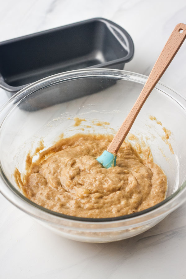 A glass bowl with batter and a blue rubber spatula.