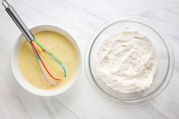 Bowl of liquid ingredient with a rainbow whisk and glass bowl of dry ingredients.