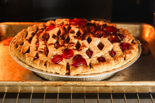 Pie baking in toaster oven with bubbly fruit and burnt spots on crust.