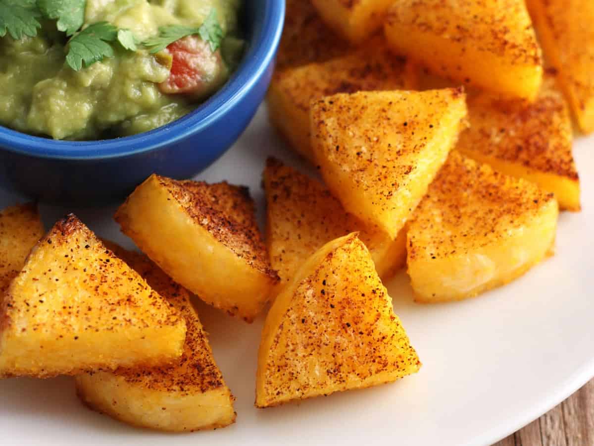 Closeup of seasoned polenta wedges on a plate with a small bowl of guacamole.