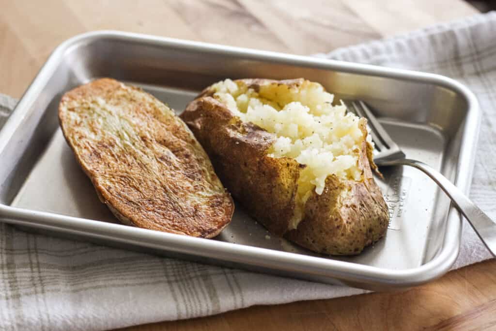 Small sheet pan with cooked potato halves fluffed with a fork.