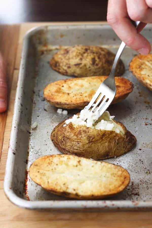 Quick baked potatoes sliced open and fluffed with a fork on a baking sheet.