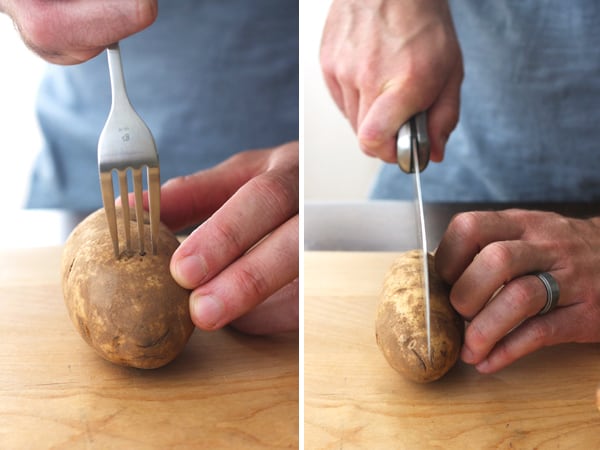 Potato stabbed with a fork and sliced in half on a cutting board.