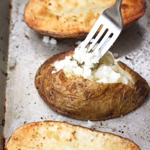 Baked potato halves on a baking sheet with one sliced open and fluffed with a fork.
