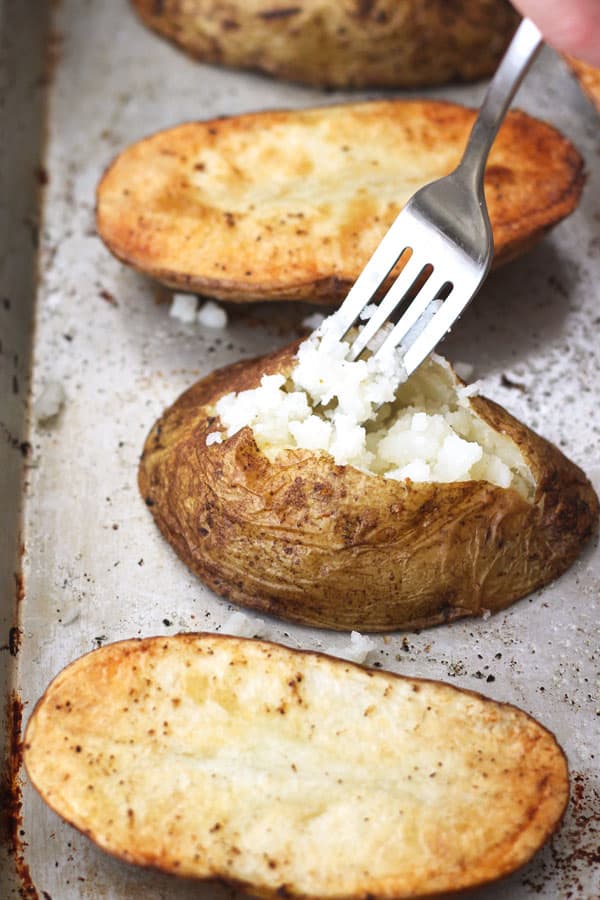 Closeup of baked potato halves on a baking sheet sliced open and fluffed with a fork.