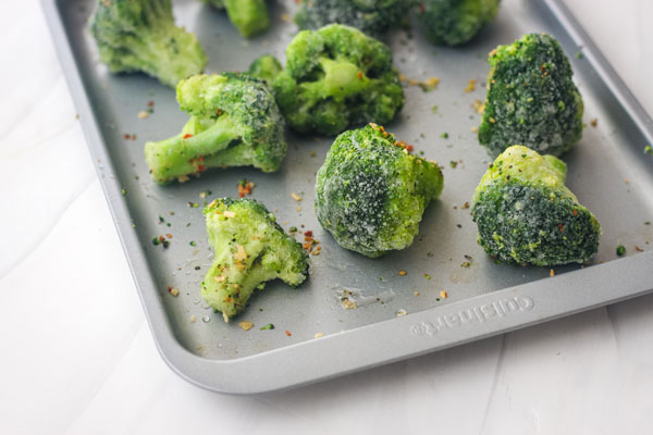 Frozen broccoli florets spread out on a baking sheet.