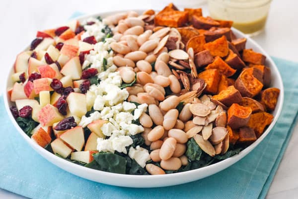 Large bowl of kale salad topped with rows of cheese, beans, and sweet potato pieces.