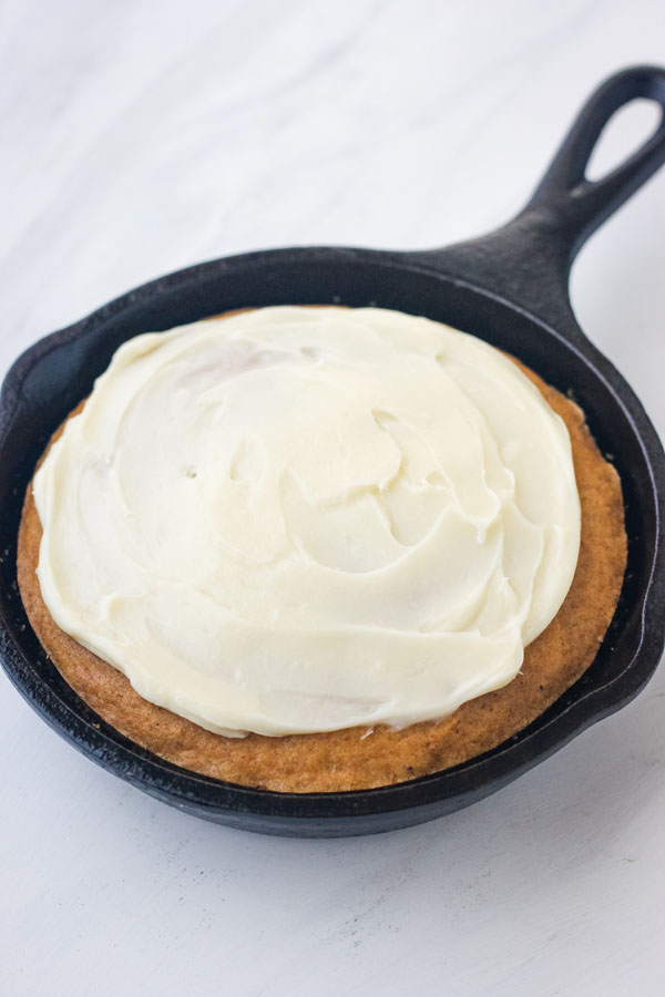 A mini pumpkin skillet cake topped with a rich cream cheese frosting on a marble background.
