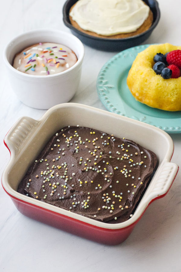 A small square chocolate cake, mini lemon bundt, and white ramekin with cake on a table.