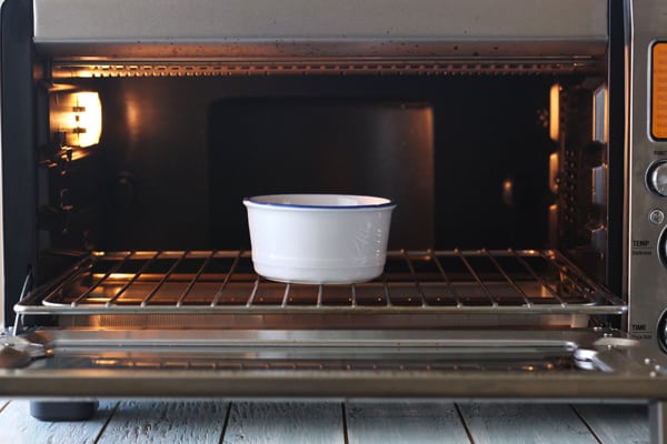 Oven-safe ramekin warming ingredients in a toaster oven.