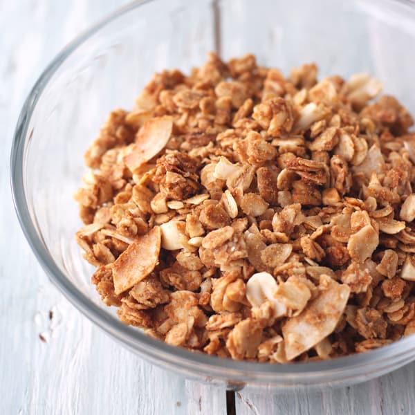 Flaky stirred granola in a glass bowl.