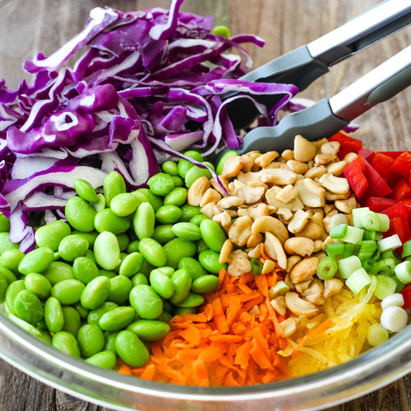 Purple cabbage, edamame, cashews, carrots, and spaghetti squash in a large glass bowl.