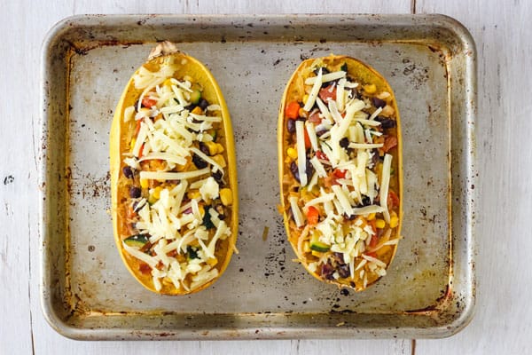 Spaghetti Squash Burrito Bowls are a hearty vegetarian dinner for two. Cheesy, flavorful, and stuffed with healthy veggies - enjoy comfort food that’s actually good for you! Overhead view of stuffed spaghetti squash halves topped with shredded cheese.