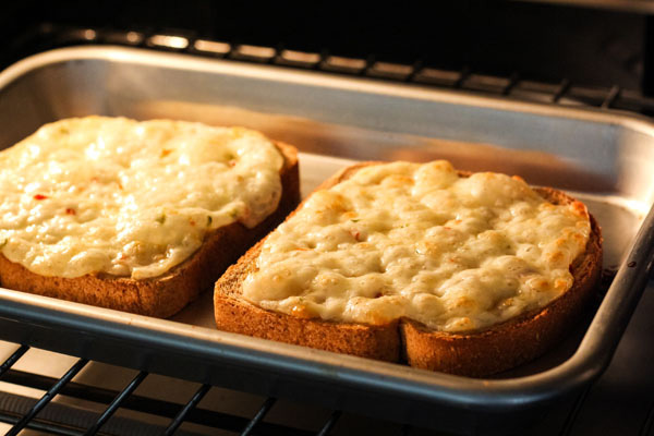 Melted cheese bubbling on bread slices inside a toaster oven.