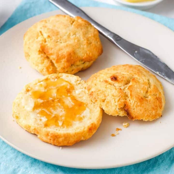 Plate of golden brown biscuits spread with butter and honey.