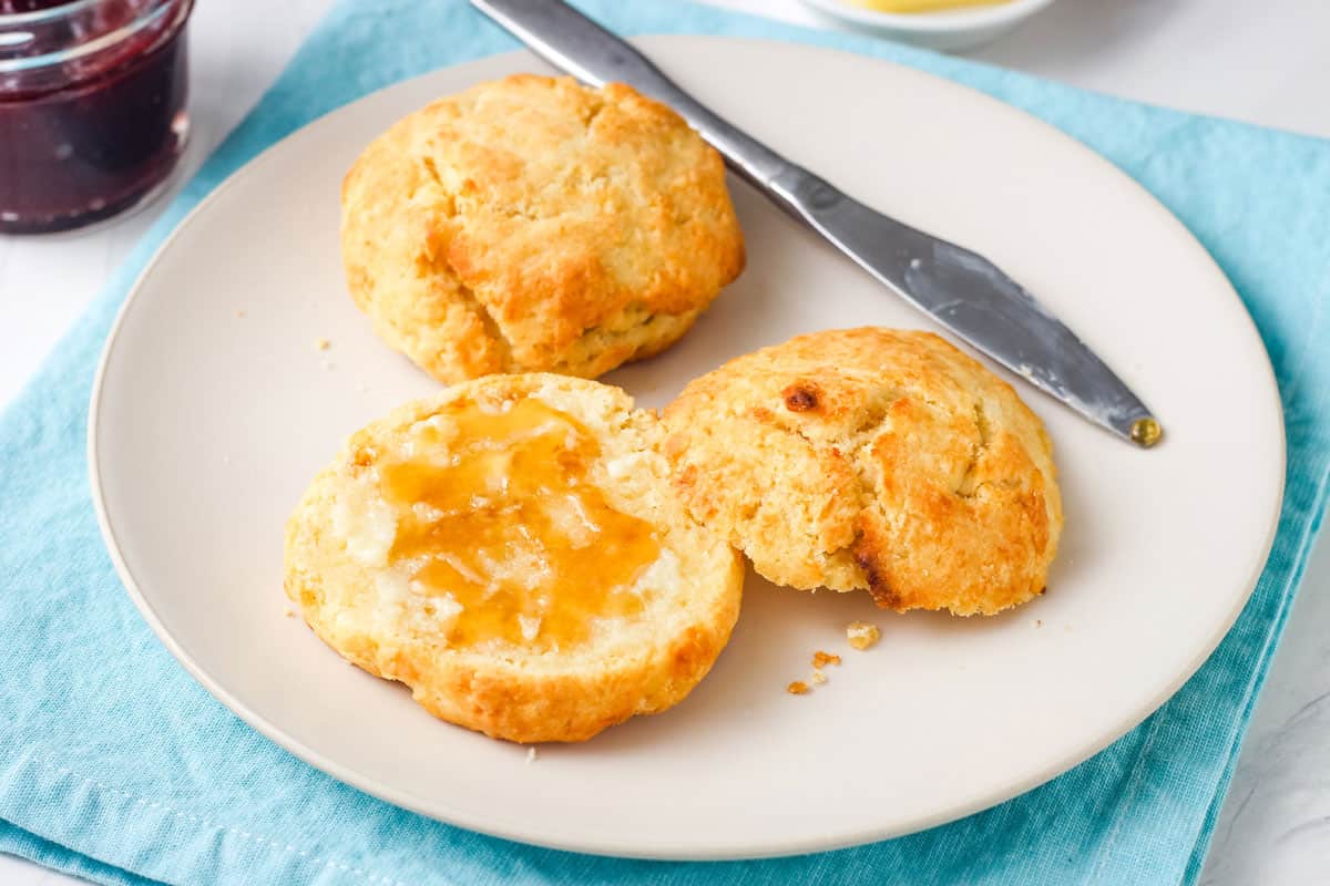 Plate of golden brown biscuits spread with butter and honey.
