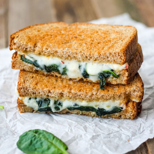 Two sandwich halves oozing melted cheese on a piece of parchment paper.