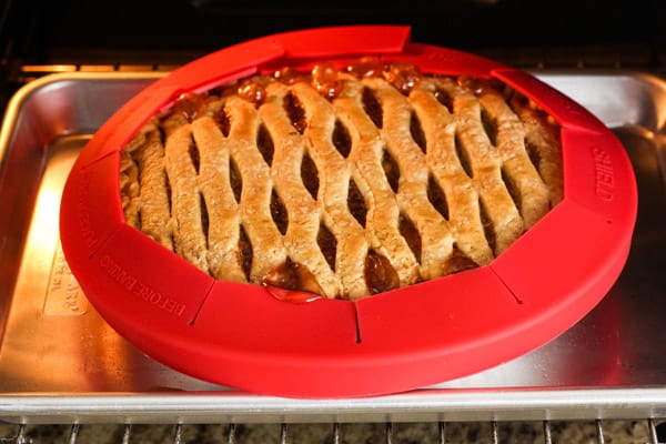 Sheet pan with apple pie covered with a red pie shield.