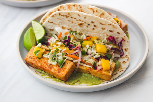Tofu tacos on a blue plate with lime wedges.
