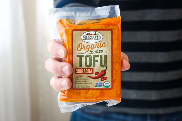 A hand holding a package of sriracha baked tofu.