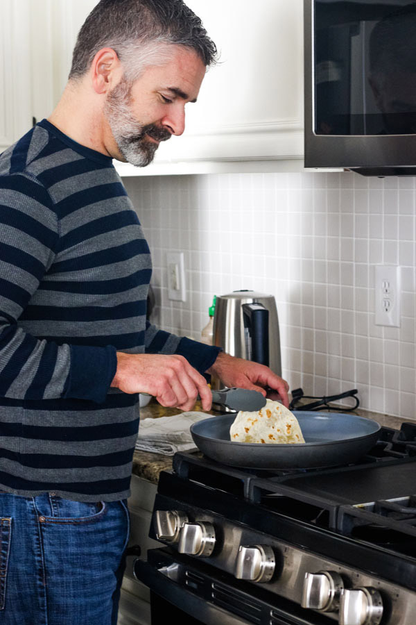 Man warming tortillas in a skillet on a stovetop.