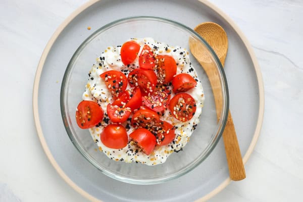 Small bowl of cottage cheese with sliced grape tomatoes and seasoning.