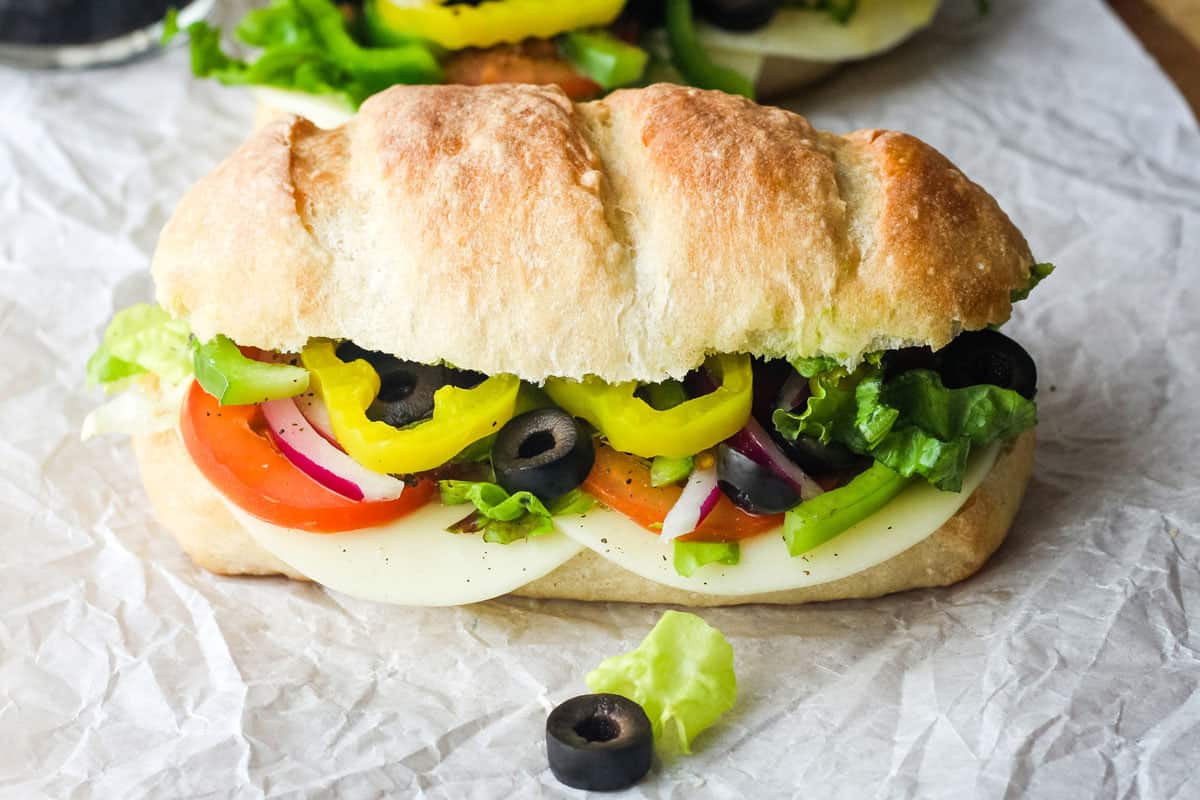 Close up of black olive slices and yellow peppers in a small sub sandwich.