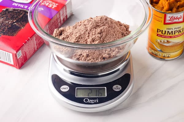 Glass bowl with dry cake mix on a kitchen scale.