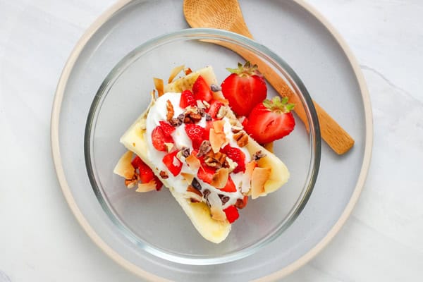 Glass bowl with half a sliced banana topped with yogurt, strawberries, and toasted coconut.