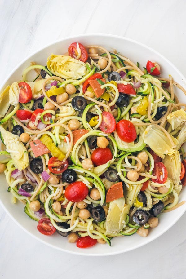 Overhead view of a big bowl of zucchini pasta salad on a white table.