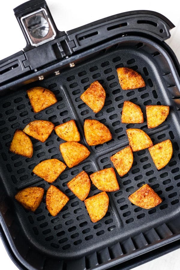 Crispy seasoned polenta wedges in an air fryer basket.
