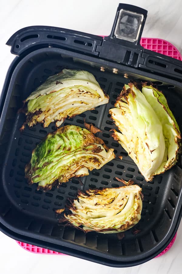 Overhead view of browned cabbage wedges in an air fryer basket.