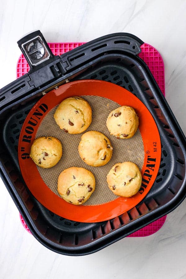 Baked golden brown cookies on a silicone mat inside an air fryer basket.