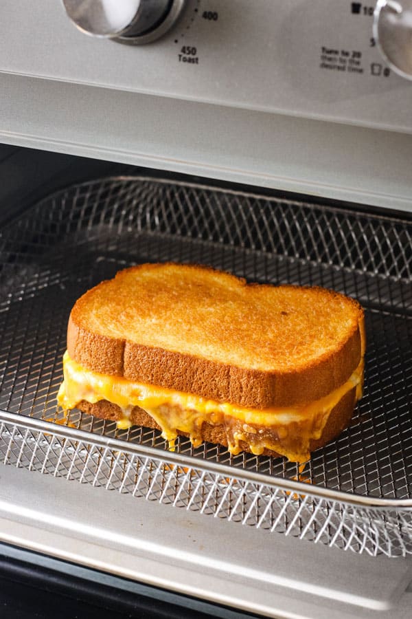 Cheesy sandwich in a metal basket inside of an air fryer toaster oven.