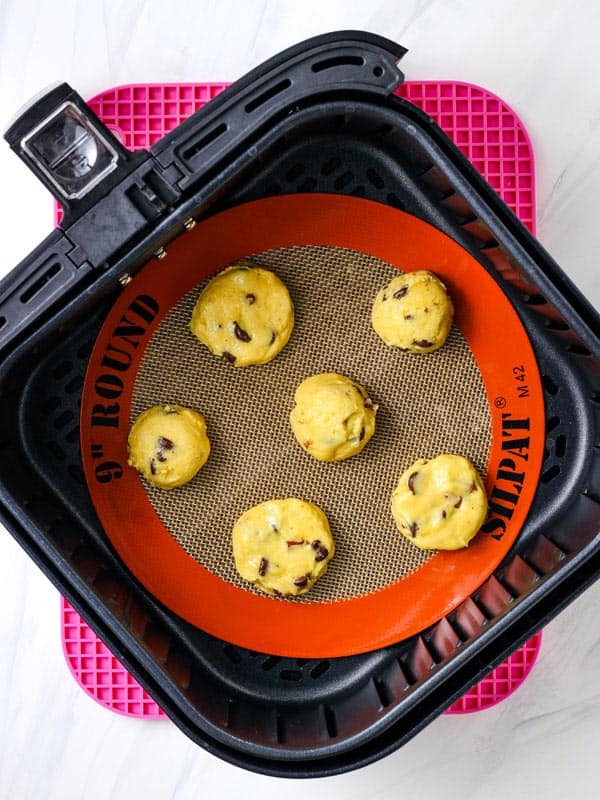 Raw cookie dough scoops in a lined air fryer basket.