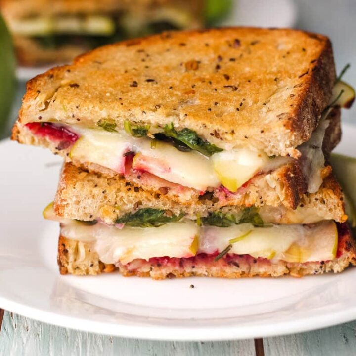 Gooey sandwich slices stacked on a plate with piece of green apple.