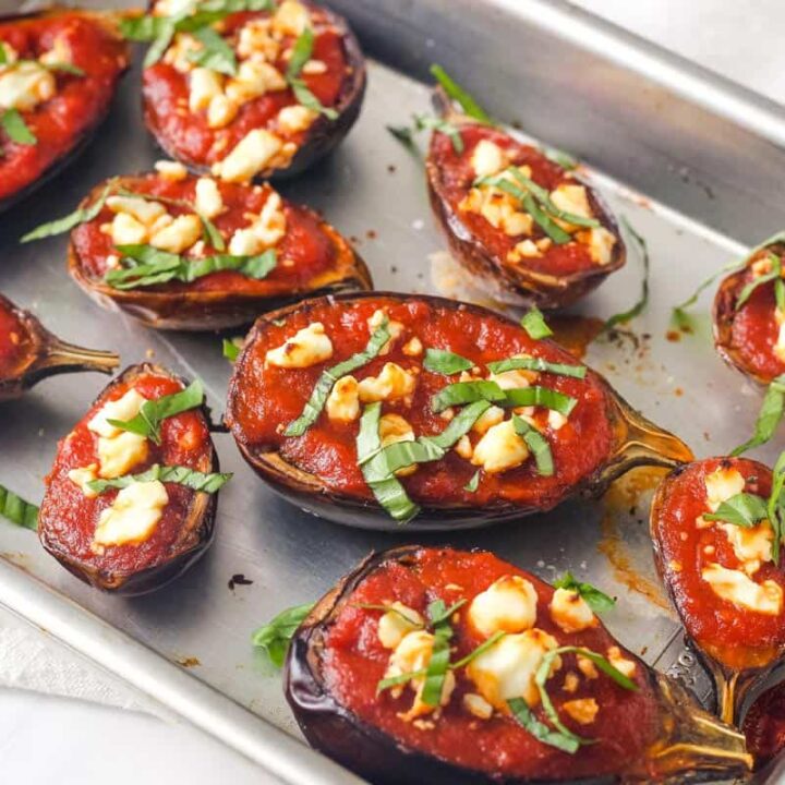 Pan of roasted mini eggplants topped with marinara, feta, and basil.