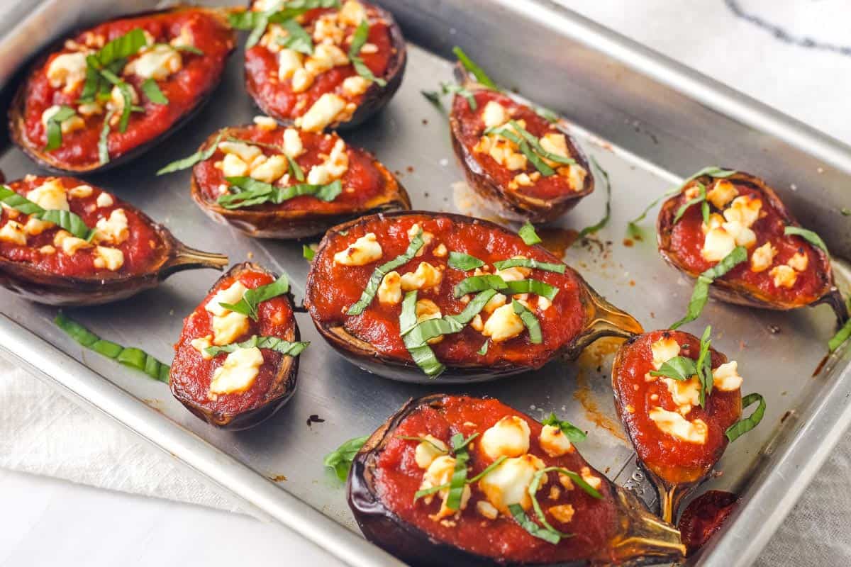 Pan of roasted mini eggplants topped with marinara, feta, and basil.
