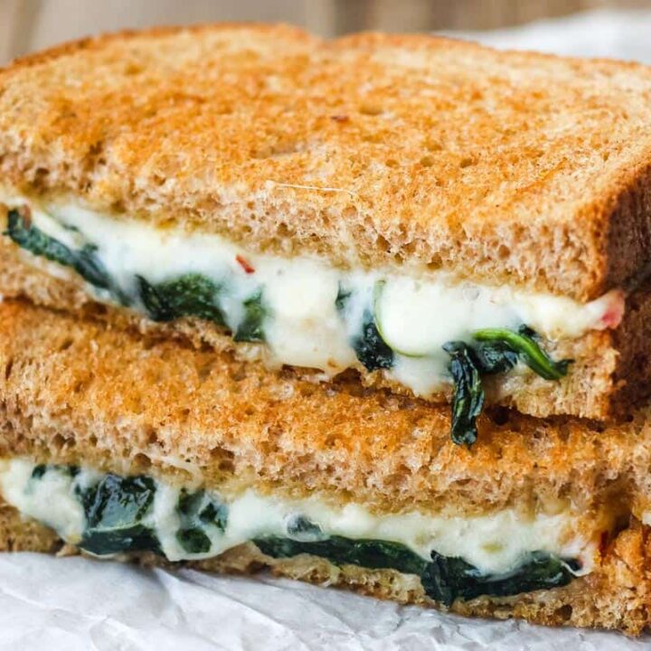 Closeup of gooey melted cheese and spinach inside a baked grilled cheese sandwich.